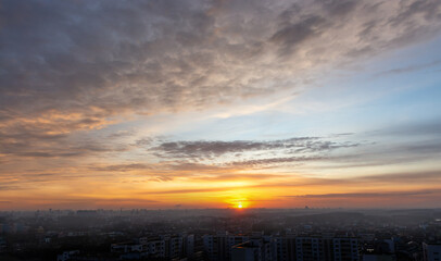 Beautiful sunset sky over the city. The sun over city houses. Bird's-eye. Blue sky and yellow clouds. Wide panorama.