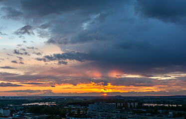 Beautiful sunset sky over the city. The sun over city houses. Blue sky and yellow clouds. Wide panorama.