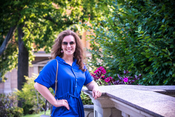 Beautiful young smiling woman in sunglasses in city park at summer day wearing dress and looking to the camera