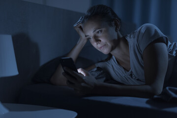Woman lying in bed at night and connecting with her phone