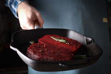 Male chef holds pan with raw beef steaks, close up