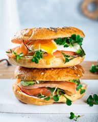 Healthy freshly baked bagel filled with salmon, microgreen, avocado and egg. Served on white desk. Sandwich with salmon. Healthy breakfast.