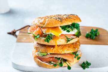Healthy freshly baked bagel filled with salmon, microgreen, avocado and egg. Served on white desk. Sandwich with salmon. Healthy breakfast.
