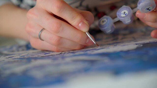 Close up of a young woman artist hand painting a picture by numbers. Creativity and art relieve stress. Hobby at home