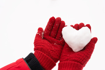 Close-up view stock photography of small white snow heart in hands of woman. Female hands in warm red gloves holding cute snowy heart. Love to winter season, St. Valentine's Day, Christmas concept