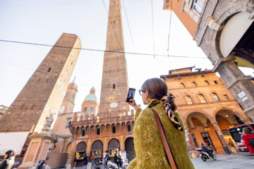 Woman photographing on phone famous Asinelli towers while traveling in Bologna city. Concept of visiting Italian landmarks in Emilia Romagna region © rh2010