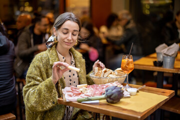 Woman eating italian meat appetizer, various sliced meat and cheese with bread and Aperol Spritz at...