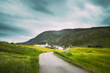 Alnesgard, Godoya, Norway. Road In Alnesgard, Godoya. Old Houses In Summer Day In Godoy Island Near Alesund Town.Alnesgard, Godoya, Norway. Road In Alnesgard, Godoya. Old Houses In Summer Day In Godoy