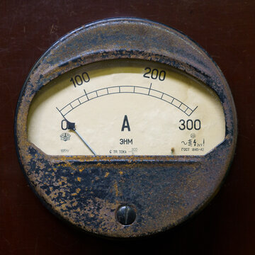 An ancient ammeter mounted on a textolite plate. Old electric current meter on a brown background. 