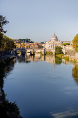 Landscape of Tiber river and green surroundings at sunny morning in Rome. Dome of famous saint Peter basalica on the skyline. Traveling Italy