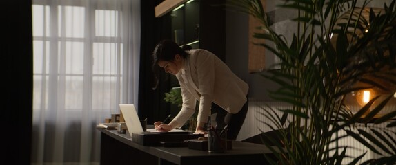 Portrait of 40s Caucasian female businesswoman looking through papers while talking on the phone in...
