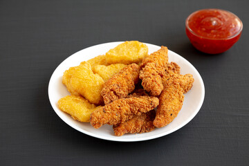 Homemade Nuggets and Chicken Tenders with Sweet and Sour Sauce on a black background, side view.