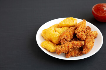 Homemade Nuggets and Chicken Tenders with Sweet and Sour Sauce on a black background, side view. Copy space.