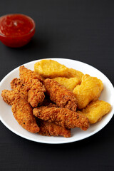 Homemade Nuggets and Chicken Tenders with Sweet and Sour Sauce on a black background, side view.