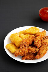 Homemade Nuggets and Chicken Tenders with Sweet and Sour Sauce on a black background, side view. Copy space.