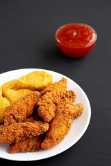 Homemade Nuggets and Chicken Tenders with Sweet and Sour Sauce on a black surface, low angle view.