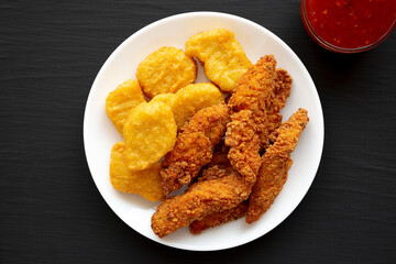 Homemade Nuggets and Chicken Tenders with Sweet and Sour Sauce on a black background, top view. Flat lay, overhead, from above.