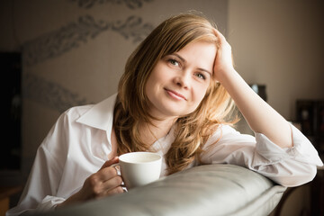 Happy smiling peaceful blond hair woman sitting on a couch at home and support her head with hand. relaxing on sofa at home