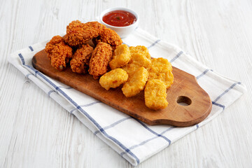 Homemade Crispy Fried Chicken Wings and Nuggets with Sweet and Sour Sauce on a rustic wooden board, side view.