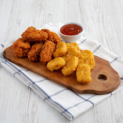 Homemade Crispy Fried Chicken Wings and Nuggets with Sweet and Sour Sauce on a rustic wooden board, side view.