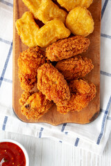 Homemade Crispy Fried Chicken Wings and Nuggets with Sweet and Sour Sauce on a rustic wooden board, view from above. Flat lay, top view, overhead.
