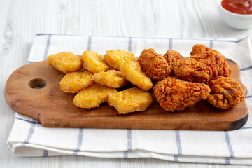 Homemade Crispy Fried Chicken Wings and Nuggets with Sweet and Sour Sauce on a rustic wooden board, side view. Close-up.