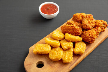Homemade Crispy Fried Chicken Wings and Nuggets on a rustic wooden board on a black background, side view.  Copy space.