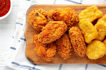 Homemade Crispy Fried Chicken Wings and Nuggets with Sweet and Sour Sauce on a rustic wooden board, view from above. Flat lay, top view, overhead.