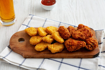 Homemade Crispy Fried Chicken Wings and Nuggets on a rustic wooden board, side view.