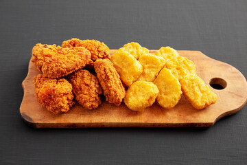 Homemade Crispy Fried Chicken Wings and Nuggets on a rustic wooden board on a black background, side view.