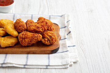 Homemade Crispy Fried Chicken Wings and Nuggets with Sweet and Sour Sauce on a rustic wooden board, side view. Copy space.