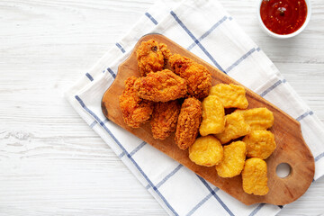 Homemade Crispy Fried Chicken Wings and Nuggets with Sweet and Sour Sauce on a rustic wooden board, top view. Flat lay, from above, overhead. Copy space.