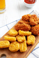 Homemade Crispy Fried Chicken Wings and Nuggets on a rustic wooden board, side view.