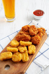 Homemade Crispy Fried Chicken Wings and Nuggets on a rustic wooden board, low angle view.