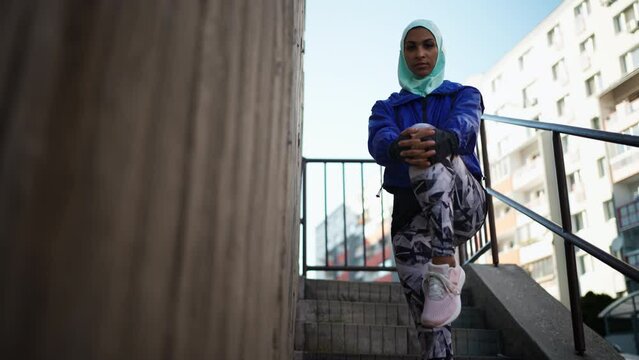 Low angle view of sporty young Muslim woman in hijab exercising outdoors in city.