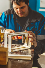 Young Caucasian carpenter in working clothes makes wooden boxes in carpentry workshop. Real scene. Workflow. Small business. Environmentally friendly packaging and containers.