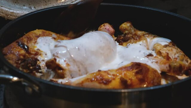 Stirring coconut milk into red thai chicken curry cooking on a stove