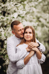 Young loving couple in a walk in a spring blooming apple orchard. Happy married couple enjoy each other while walking in the garden. Man holding woman's hand