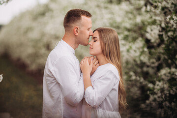 Fototapeta premium Young loving couple in a walk in a spring blooming apple orchard. Happy married couple enjoy each other while walking in the garden. Man holding woman's hand