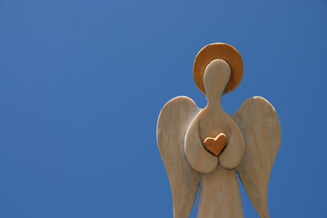 Wooden angel on blue sky background. Religious postcard. Copy space. 