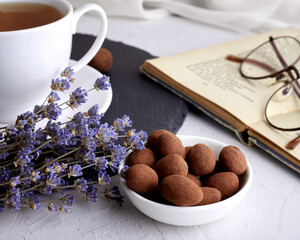 Chocolates and a bunch of lavender. In the background is a cup of tea and an open book with glasses on it. Color of the Year 2022 Very Peri