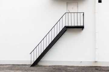 A black metal staircase against a white wall with a closed door.
