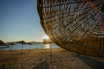 The beautiful sun at sunset shines through a beach umbrella overlooking the sea. - 484128181
