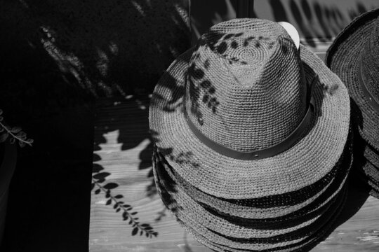 Stack of classic straw men's hats. Street trade. Shopping tourism in France. Bright sun in harsh shadows. Black and white photo. 