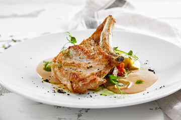 Roasted pork steak with vegetables garnish and sauce. Bone-in ribeye pork chops. Main course of pork in rustic style.