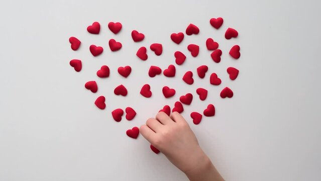  Heart made of shiny red small decorative hearts on a white background with child hand