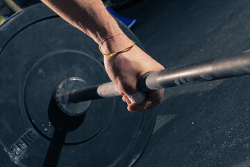 Closeup of man's left hand with bracelet hook gripping a barbell with 20kg plates
