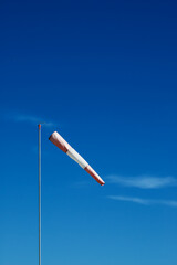 Red and white windsock on a metal pole on blue sky background with cirrus clouds