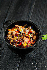Yakisoba noodle with chicken and vegetables on wooden background. Japanese stir fry noodles in wok on black table with ingredients. Chicken with buckwheat soba on wok. Oriental cuisine. Wok menu.