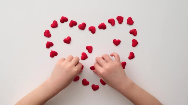  Heart made of shiny red small decorative hearts on a white background with child hands